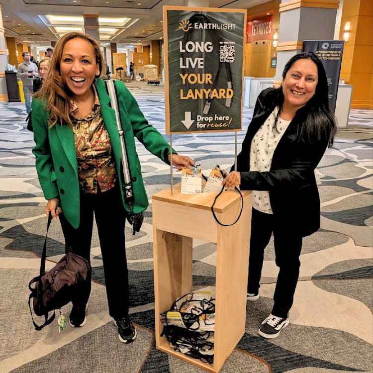 Two expo, meeting and event attendees dropping lanyards into floor-standing wooden collection box for sustainable Second Life Lanyard collection program for lanyard rental, reuse, repurose