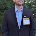 Person wearing branded wood name tag holder 4" x 3" for Node Climate sustainable event with reusable metal double clip